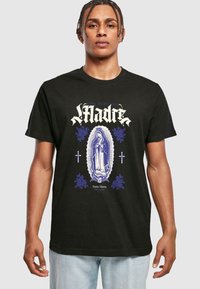 Zwarte katoenen t-shirt met een centraal blauw en wit grafisch ontwerp van een religieuze figuur, omringd door bloemaccenten en tekst in gestileerd lettertype.