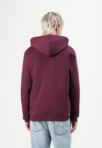Bordeaux hoodie met een trekkoordcapuchon, lange mouwen en een geribde zoom. De stof lijkt zacht met een gladde textuur.
