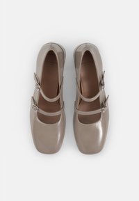 Chaussures Mary Jane en cuir verni beige avec deux brides ajustables et orteils carrés, présentant une finition texturée et des accents lisses.