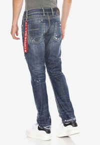 Dunkelblaue Denim-Jeans mit einzelnen used-Effekten, weißen Nähakzenten und einem roten Markenetikett an der Tasche. Sie verfügen über einen schmalen Schnitt.
