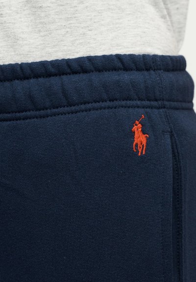 Περιοχή μέσης σε μπλε ναυτικό φορμά με ελαστική ζώνη και ένα μικρό κόκκινο κεντημένο λογότυπο παίκτη πόλο κοντά στην πλαϊνή τσέπη.