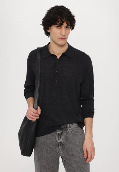 Polo shirt à manches longues gris foncé avec col et patte de boutonnage à trois boutons, associé à un jean texturé gris clair. Sac à bandoulière noir.