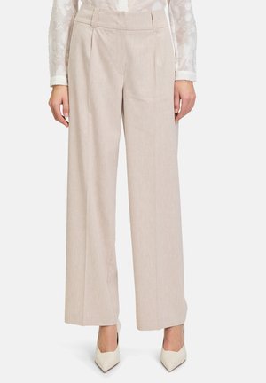 Wide-leg beige trousers with pleats, crafted from a textured fabric. Styled with a high waist and worn with pointed white heels.