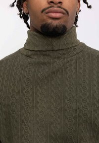 Pull en laine vert olive à col roulé, présentant un motif texturé avec des motifs en zigzag surélevés et un col haut pour la chaleur.
