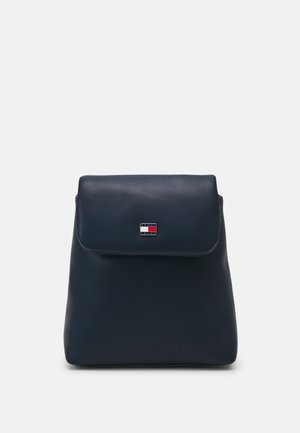 Sac à dos en cuir bleu foncé avec une fermeture à rabat et un petit logo rectangulaire aux couleurs rouge, blanc et bleu au centre devant.