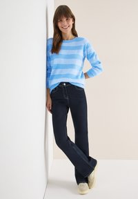 Maglione a righe azzurro chiaro realizzato in materiale morbido e strutturato, abbinato a pantaloni denim scuro a zampa con cuciture a contrasto e vestibilità slim.