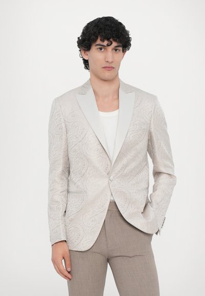 Light beige blazer with a paisley pattern, satin shawl lapels, and a single button closure. Complemented by a plain white shirt and beige trousers.