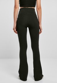 Leggings noirs taille haute avec une coupe ajustée, finitions évasées, texture lisse et sans motifs ni détails métalliques visibles.