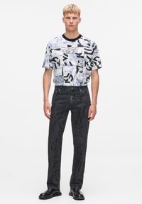 Tricou grafic cu un design abstract alb-negru, combinat cu blugi negri cu un model subtil, completat cu cizme negre.