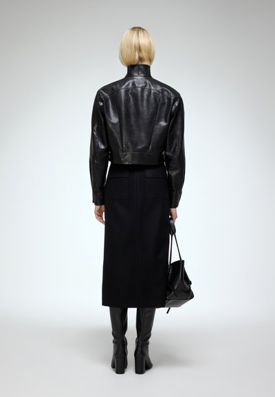 Černá kožená cropped bunda s vysokým límcem a úzkým pasem; v kombinaci s dlouhou černou sukní, černými kozačkami po kolena a černou kabelkou.