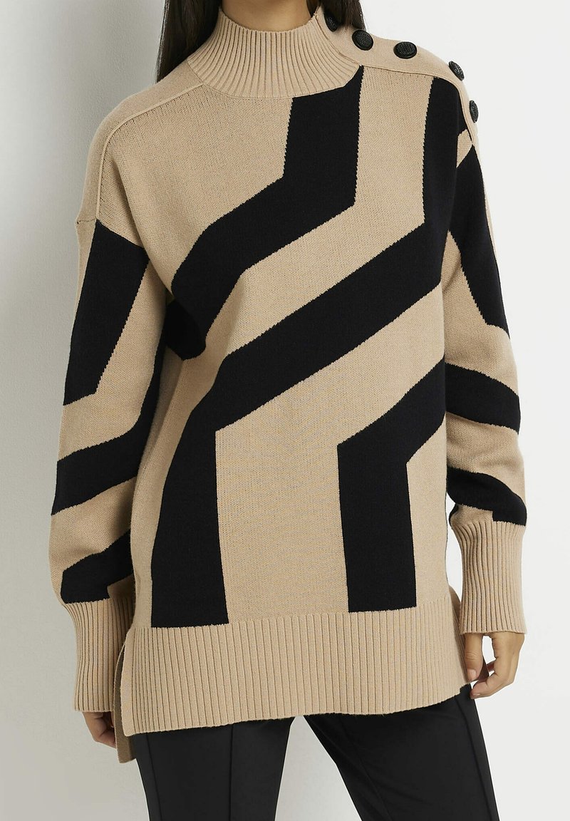 Beige gebreide trui met zwarte zigzagpatronen, ribbelhalslijn en accenten. Bevat schouderknopen en zijsplitsen voor extra comfort.