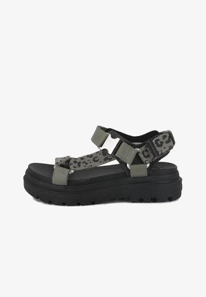 Crna sandala na platformu s debelim potplatom, maslinasto zelenim remenima s leopard uzorkom i velikom srebrnom kopčom sa strane.