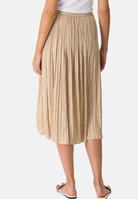 Gonna midi plissettata in beige chiaro con vita elastica. Il tessuto morbido aggiunge texture al design fluido, che arriva a metà polpaccio.