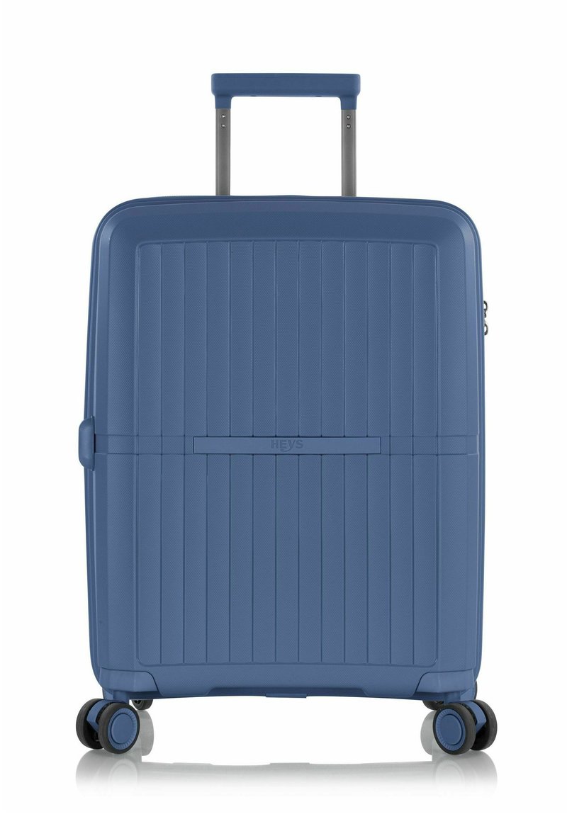 Valigia rigida blu con texture a righe verticali, manico retraibile, quattro ruote e un compartimento con zip. Presenta il marchio HEYS.