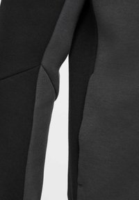 Sudadera asimétrica en gris oscuro y negro, hecha de una tela suave y texturizada, con un diseño de paneles angulados en contraste.