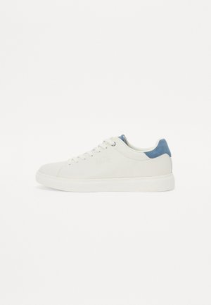White sneaker made of smooth leather with a textured navy blue accent on the heel. Features laces and a rubber sole. Minimalist design.