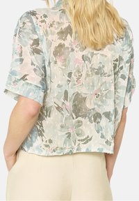 Short-sleeved, cropped blouse in lightweight, sheer fabric. Features a floral pattern with green, pink, and blue hues. Textured finish.