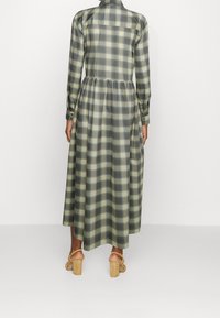 Lång rutigt klänning i grön och beige, med knäppning fram, långa ärmar och en rynkad midja, tillverkad av lättviktsmaterial.
