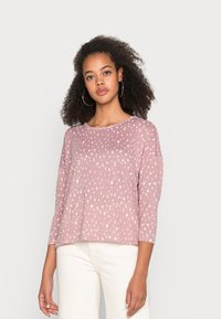 Blusa de algodão rosa com mangas a três quartos, apresentando um padrão de bolinhas brancas e um decote redondo, exibida sobre um fundo neutro.