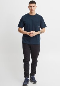 Navy blue short-sleeve t-shirt with a chest pocket, paired with black sweatpants, and navy blue athletic shoes. Simple design and relaxed fit.