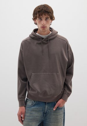 Hoodie en coton marron avec une poche frontale, capuche à cordon de serrage et poignets côtelés. Association avec un jean en denim délavé.