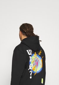 Sudadera negra con una gráfica vibrante de baloncesto con llamas y el texto "wn?" impreso en la parte posterior. Mezcla de algodón, corte relajado.