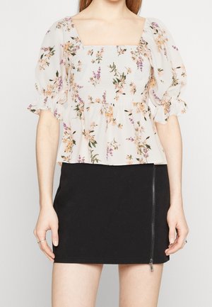 Blusa a stampa floreale con scollo quadrato, maniche a palloncino e corpetto smock; abbinata a una mini gonna nera con dettaglio della cerniera laterale.