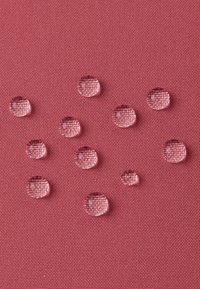 Gocce d'acqua su una superficie tessile rosa e strutturata, che rivelano la trama del tessuto e illustrano la resistenza all'acqua.