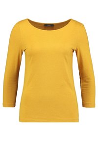 Halenka s dlouhým rukávem, kulatým výstřihem a těsným střihem vyrobená z měkké žluté bavlny. Má bezšvová ramena a hladkou strukturu. Žádné viditelné vzory ani akcenty.