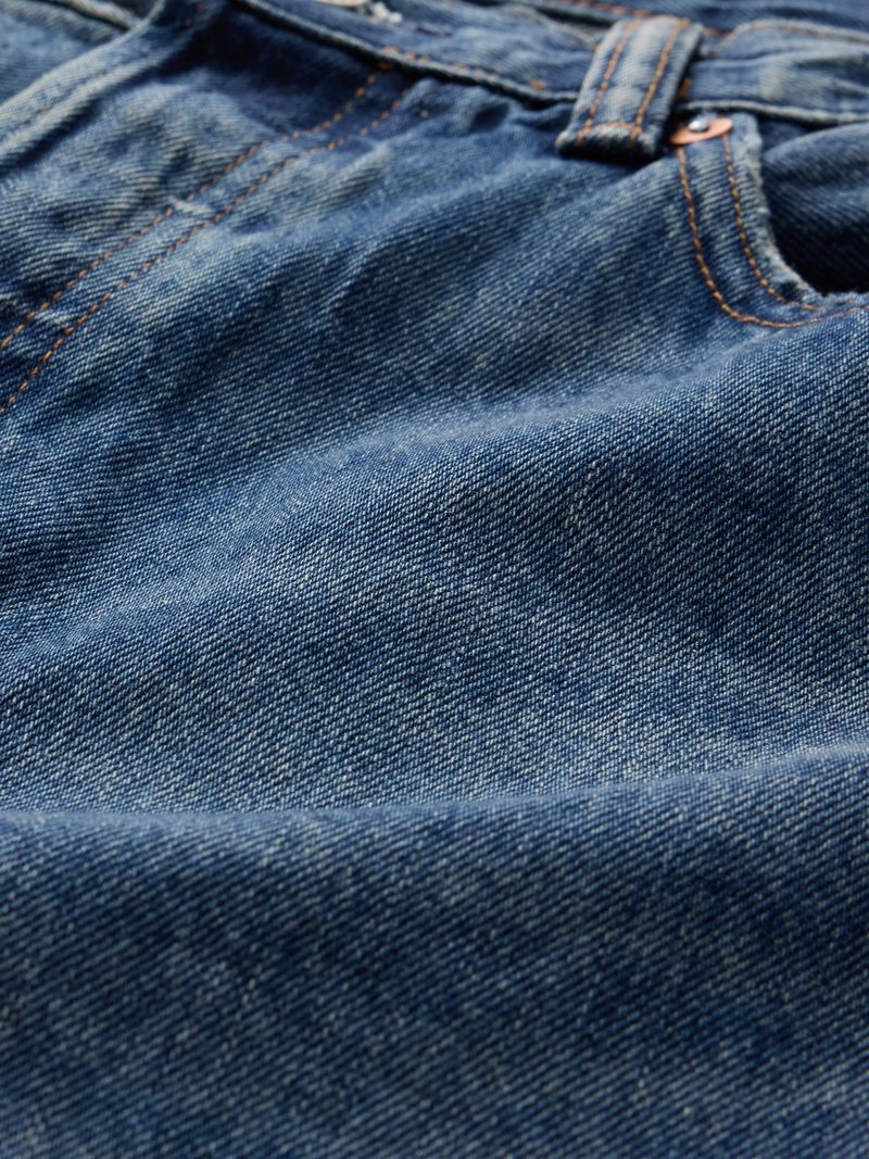 Nahaufnahme von blauer Denim-Stoff mit sichtbaren Nähten, Gürtelschlaufe und Metallniete an einer Jeans.