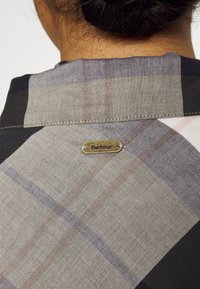 Koszula w kratę Barbour w czarno-beżowej kolorystyce, wyposażona w złoty znacznik z logo przy kołnierzyku oraz fakturowany wzór materiału.