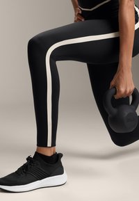 Fekete sport leggings, fehér függőleges csíkkal, fekete és fehér sportcipővel párosítva, valamint egy 8 kg-os felirattal ellátott fekete kettlebell.