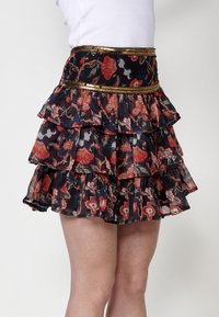 Zwarte bloemen mini-rok met meerdere ruches, versierd met rode en blauwe bloemenpatronen en een met pailletten bezette gouden tailleband.