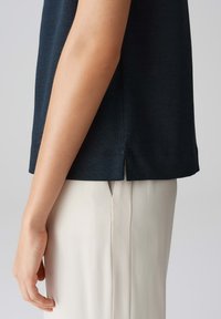 Marineblauwe katoenen t-shirt met korte mouwen, voorzien van een zijsplit aan de onderkant. Gecombineerd met crèmekleurige broeken, die een gladde textuur tonen.