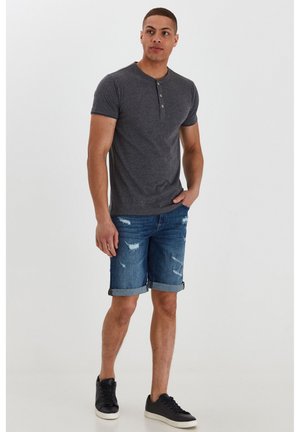 T-shirt henley gris à manches courtes et trois boutons, associé à un short en denim usé et des baskets noires basses.