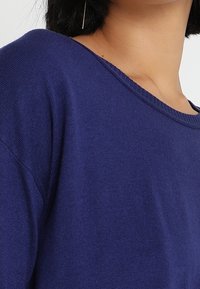 Głęboki granatowy dziany top z szerokim dekoltem i prążkowanymi detalami. Miękka faktura i luźny krój, z asymetrycznym dołem.