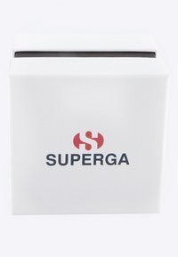 Balta dėžė su tekstūruota paviršiumi, ant kurios priekyje yra raudonas ir juodas logotipas su užrašu "SUPERGA", o viršus atidarytas, atskleisdama tamsų vidų.