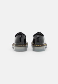 Czarne buty z lakierowanej skóry z przezroczystą gumową podeszwą i żółtym przeszyciem. Posiadają zaokrąglony nosek oraz pętelkę z tyłu ułatwiającą zakładanie.