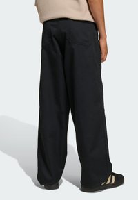 Čierne nohavice s širokými nohavicami z pevnej tkaniny, vybavené zadnými vreckami a čistým švom. Nosené s čiernymi sandálmi a béžovým topom.