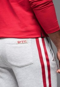 Pantalones de chándal grises con franjas laterales rojas, un bolsillo trasero y una etiqueta que dice "OMBRE". Combinados con una camiseta de manga larga roja.