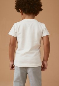 Hvid bomulds T-shirt med korte ærmer, der har en tekstureret overflade. Bagbeklædningen har en rund halsudskæring og er parret med lysegrå bukser.