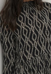 Vestido negro con una tela texturizada y bordado en crema con patrón de hojas. El escote es fruncido y el diseño fluye hacia una falda plisada.