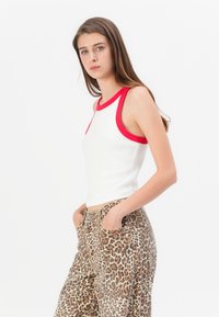 Débardeur blanc à côtes avec encolure rouge, associé à un pantalon large imprimé léopard brun clair, doté de poches latérales.