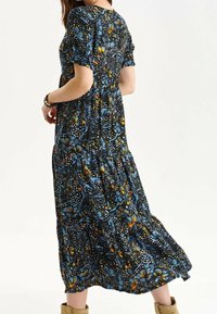 Vestido maxi con mangas cortas, con un fondo negro y patrones florales y abstractos en colores azul, amarillo y naranja.