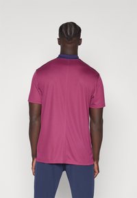 Bordowa koszulka sportowa z fioletowym kołnierzykiem, krótkimi rękawami i gładką teksturą. Ma wyraźne szwy i luźny krój.