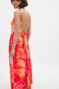 Moteris vilkinti suknelę be nugaros, be rankovių, su plonomis petnešomis ir dideliu kaspinu, surištu apatinėje nugaros dalyje, raudonai-rožinės gėlių raštų.