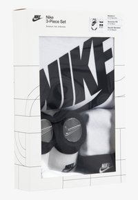 Nike 3 dalių rinkinys apima baltą bodysuitą su juodu logotipu, derančią juodą kepurę ir kojinytes. Kiekvienas daiktas turi Nike ženklinimą ir paprastą dizainą.