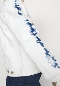 Bílé džíny bunda se indigo tie-dye akcenty na rukávech, jednoduchý design, klasický límec a kovové detaily knoflíků.