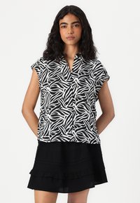 Blouse à manches courtes présentant un motif de vagues noir et blanc, avec un devant boutonné et une coupe décontractée, associée à une jupe noire à volants.