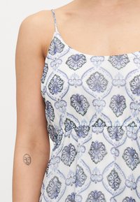Rochie albă cu un model floral în nuanțe de albastru și gri. Bretele subțiri, cu o talie strânsă și textură în țesătură.
